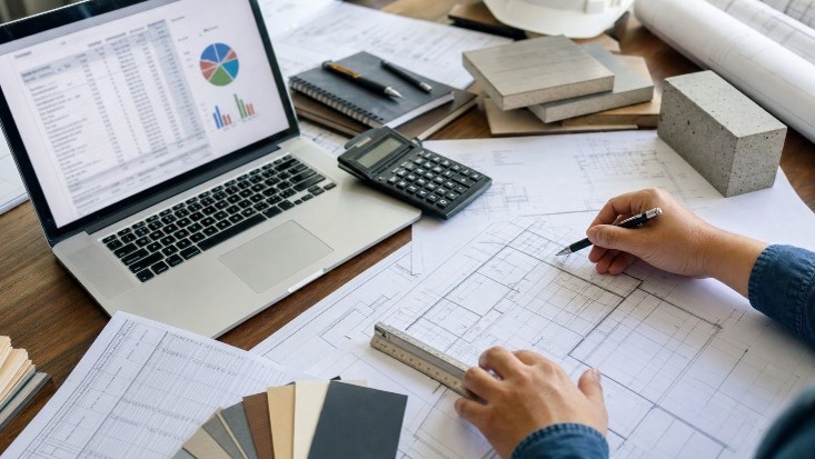 Cost estimation workspace with laptop, drawings, and ruler